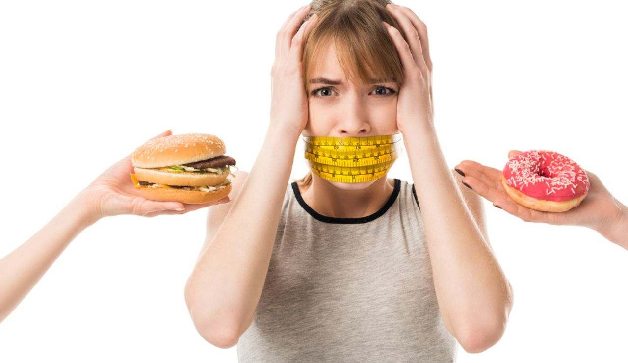Donna con metro per misurare centimetri sulla bocca e hamburger e donuts che la tentano