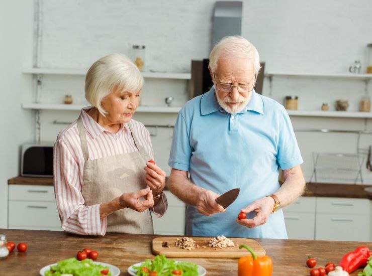 Coppia di anziani cucina insieme con tagliere in legno