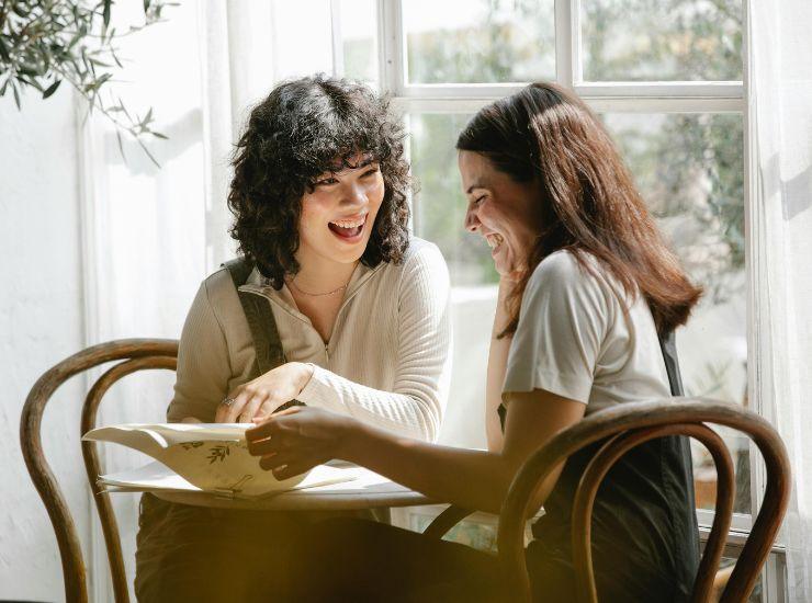 Ragazze sedute al tavolo che discutono di qualcosa in maniera divertita