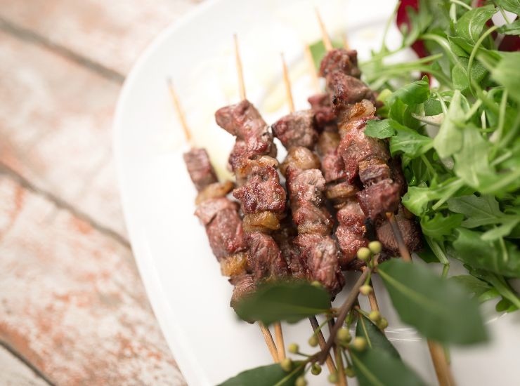 Primo piano di arrosticini adagiati su un piatto con accanto della rucola