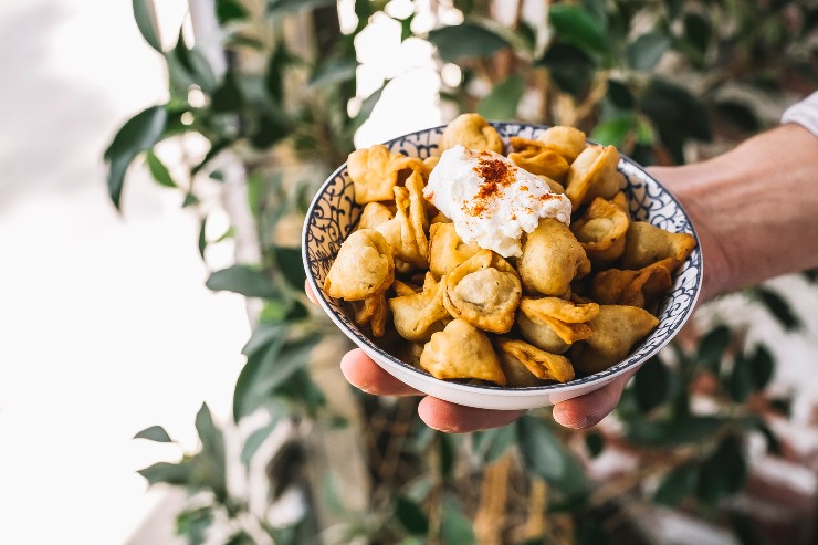 Un piatto di tortellini fritti accompagnati con panna e una spolverata di cannella 