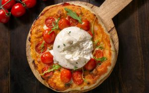 Pizza margherita con burrata su un tagliere di legno vicino a dei pomodorini