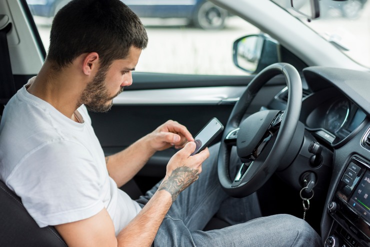 Un uomo scrive al cellulare mentre è alla guida di una macchina