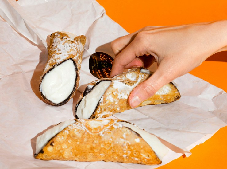 Una persona prende un cannolo siciliano da un vassoio di carta sul tavolo 